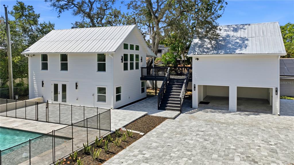 An exterior view of a white two-story house with a metal roof and paved patio — 1109 CHARLES STREET, CLEARWATER, FL