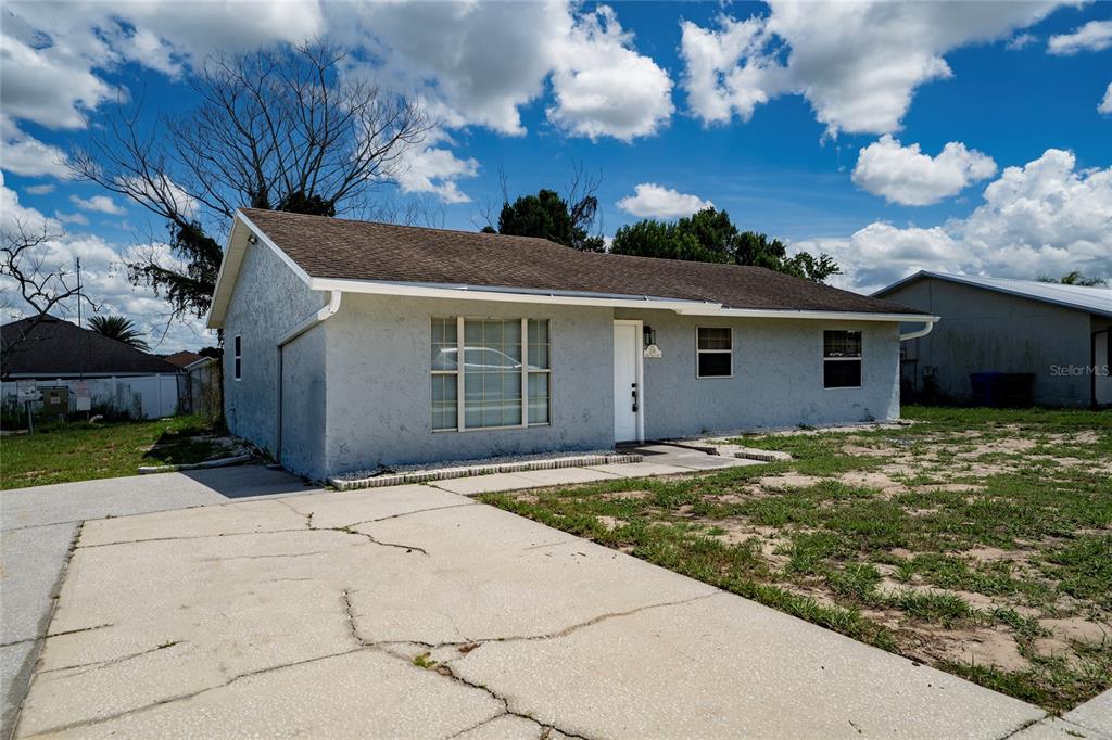 A single-story house with a gray stucco exterior, a brown roof, and a cracked concrete driveway — 276 18TH STREET NE, WINTER HAVEN, FL