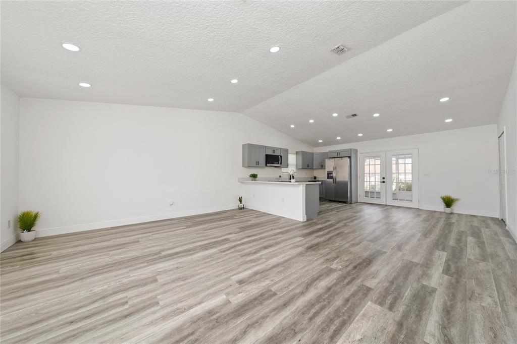 An open-concept living area features light wood-look flooring, white walls, and a kitchen with gray cabinets — 276 18TH STREET NE, WINTER HAVEN, FL