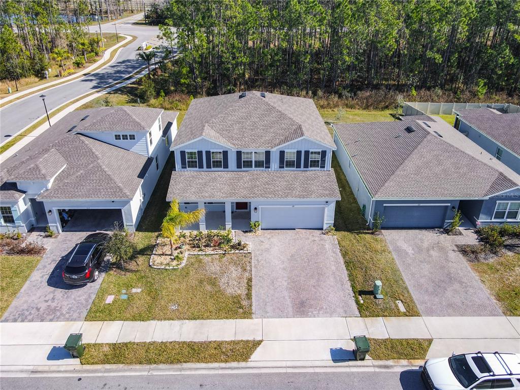 An aerial view shows three suburban houses with paved driveways and lawns along a street — 121 EAGLE HARBOR WAY, DAYTONA BEACH, FL