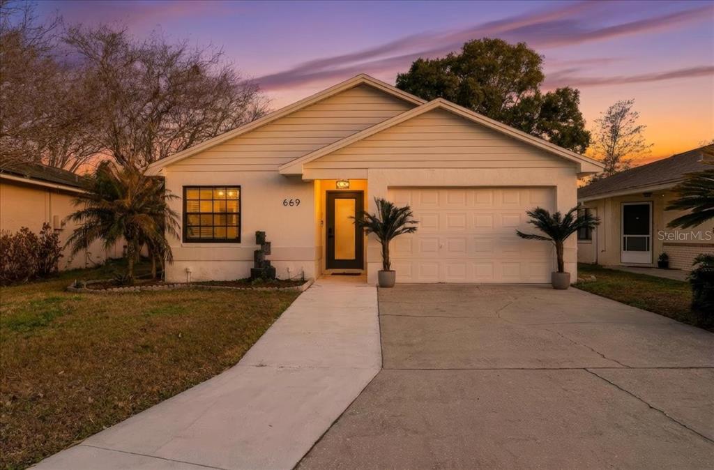 A single-story house with a white exterior, a garage, and a concrete walkway at sunset — 669 EAGLE RUN, LAKELAND, FL