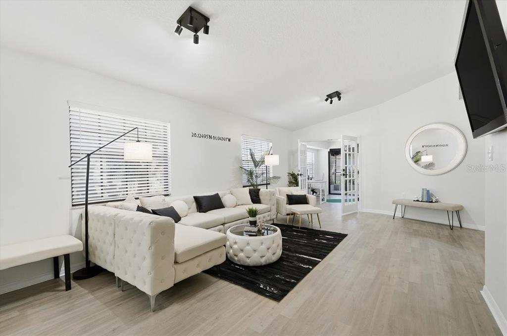 A bright living room features a white sectional sofa, a round tufted ottoman, and light-colored flooring — 669 EAGLE RUN, LAKELAND, FL