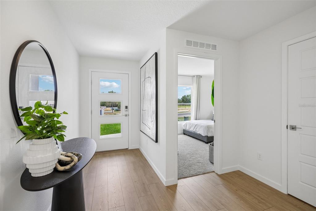 A bright entryway features light wood flooring, a modern front door, and a side bedroom — 239 SKYFIELD COURT, LADY LAKE, FL