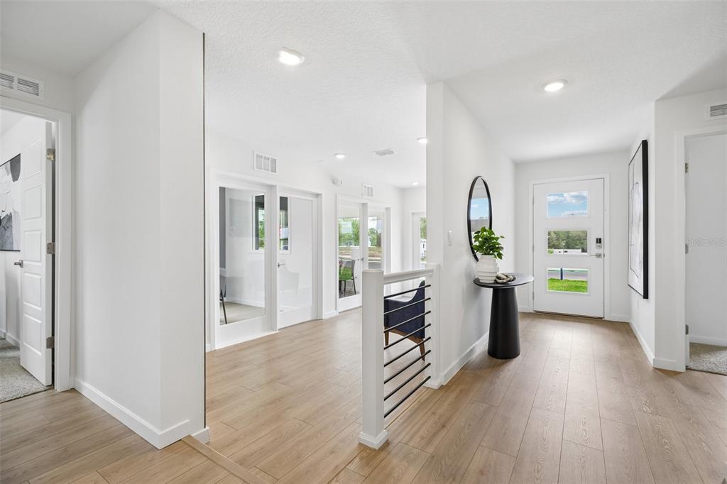 A bright entryway features light wood flooring, a white front door, and a modern staircase — 239 SKYFIELD COURT, LADY LAKE, FL