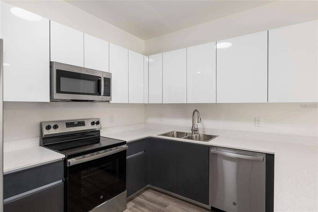 A kitchen features white upper cabinets, dark lower cabinets, stainless steel appliances, and white countertops — 1581 NW 29TH ROAD UNIT 8, GAINESVILLE, FL