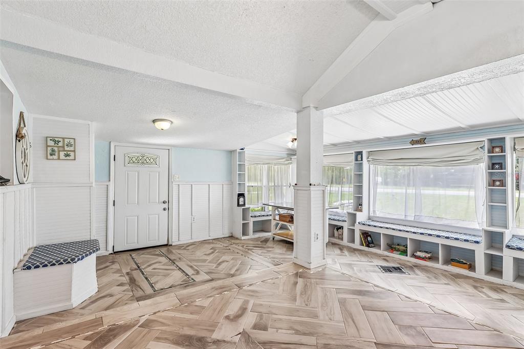 A bright sunroom features herringbone-patterned wood-look flooring, built-in window seating, and white wainscoting — 6281 BASS HIGHWAY, ST CLOUD, FL