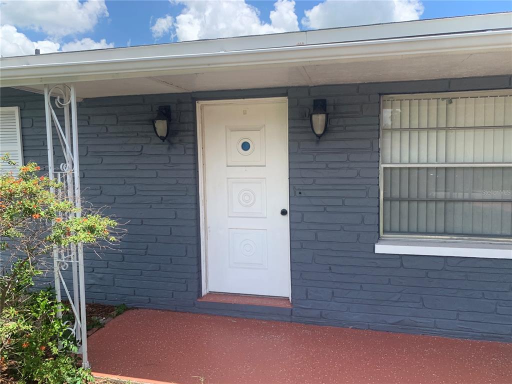 A white front door with a circular window sits on a gray brick exterior porch — 119 ALLEN AVENUE, WINTER HAVEN, FL