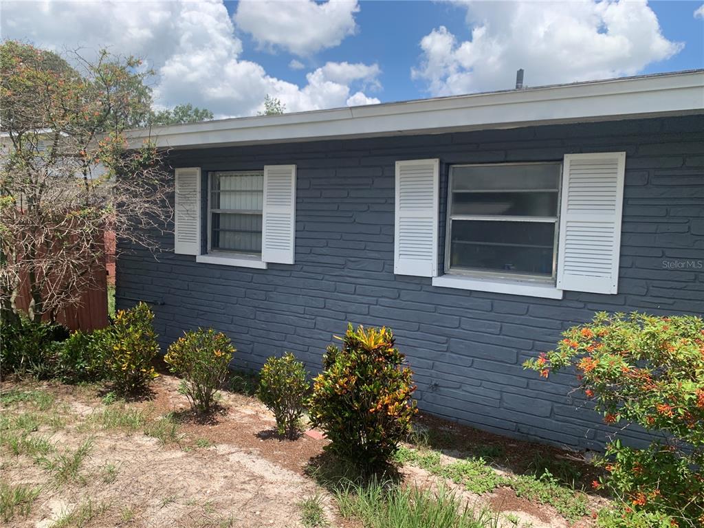 The exterior of a gray brick house features two windows with white shutters and landscaping — 119 ALLEN AVENUE, WINTER HAVEN, FL