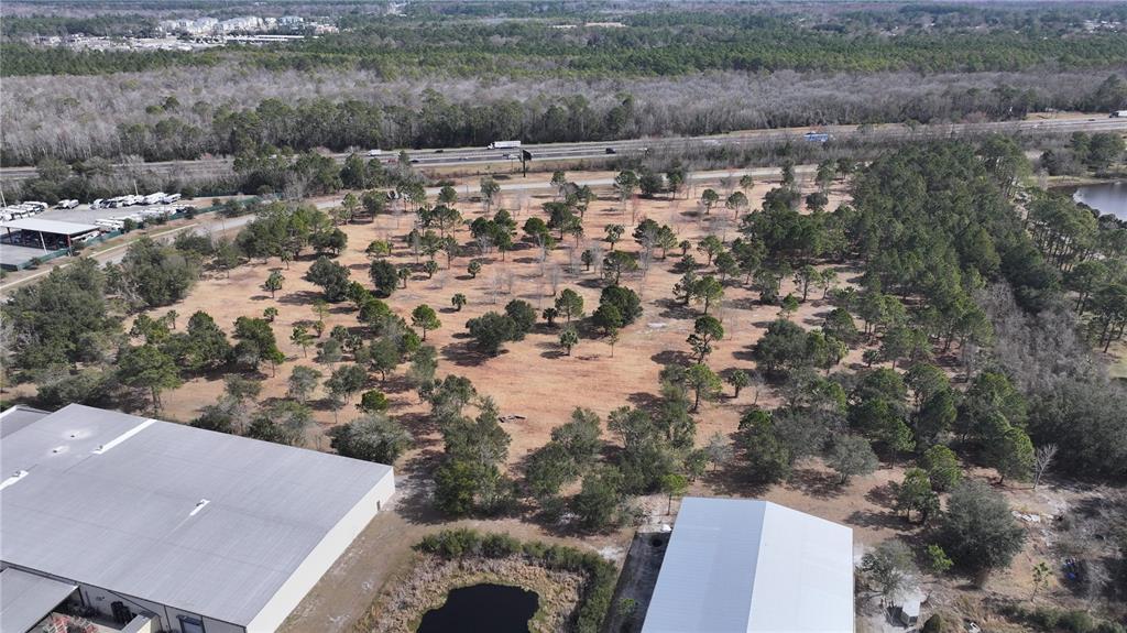 An aerial view shows a large, partially wooded lot situated between two commercial warehouse buildings — AGRICULTURAL CENTER DRIVE, ST AUGUSTINE, FL
