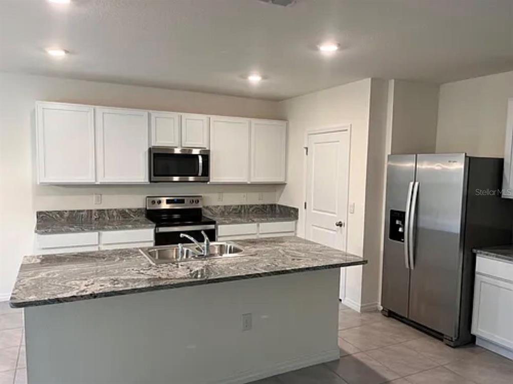 A kitchen with white cabinets, granite countertops, a center island, and stainless steel appliances — 5 HICKORY COURSE LOOP, OCALA, FL