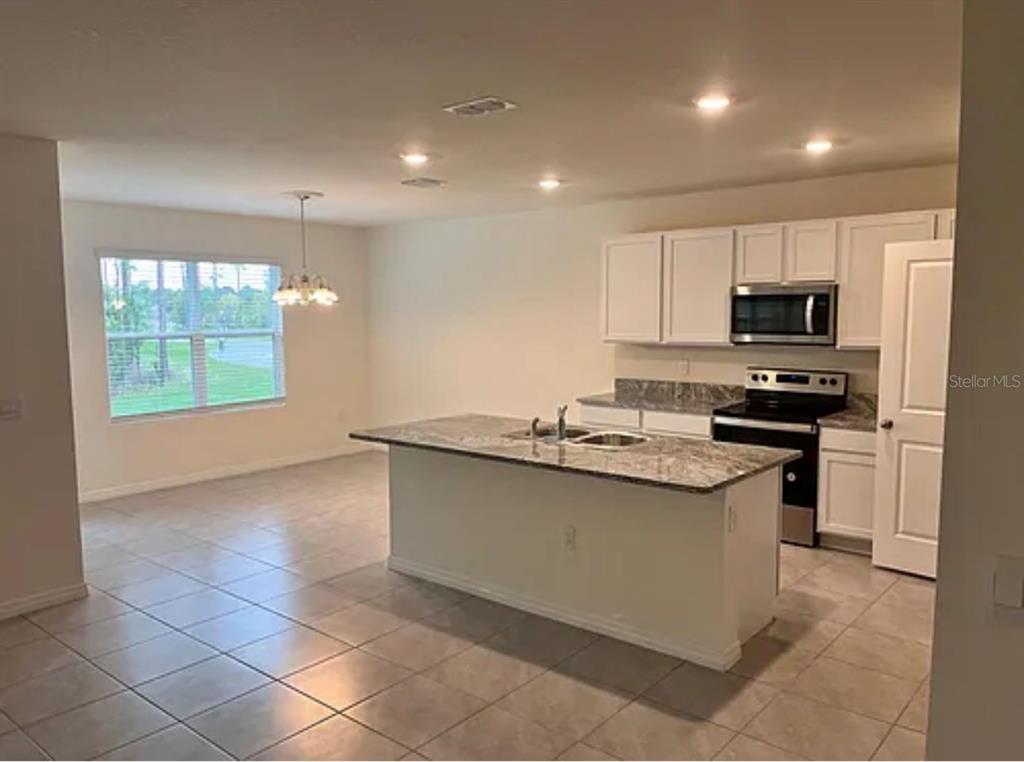 A kitchen with white cabinets, granite countertops, a center island, and an adjacent dining area — 5 HICKORY COURSE LOOP, OCALA, FL