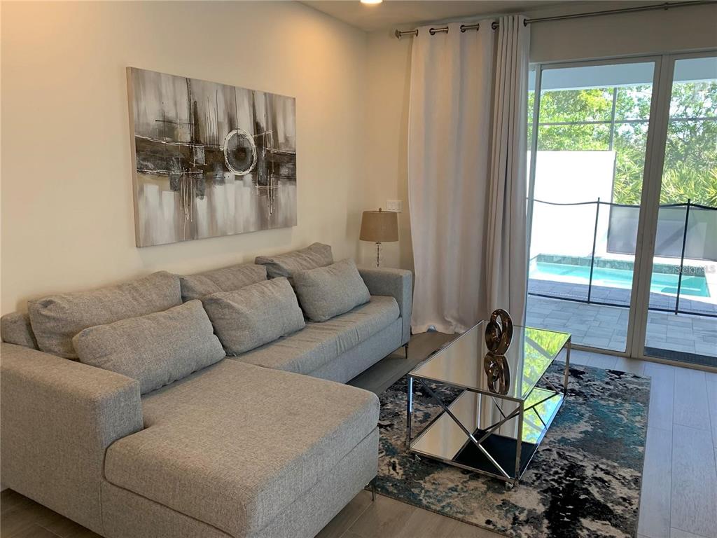 A living room with a gray sectional sofa, mirrored coffee table, and sliding door to a pool — 17307 HIDDEN FOREST DRIVE, CLERMONT, FL