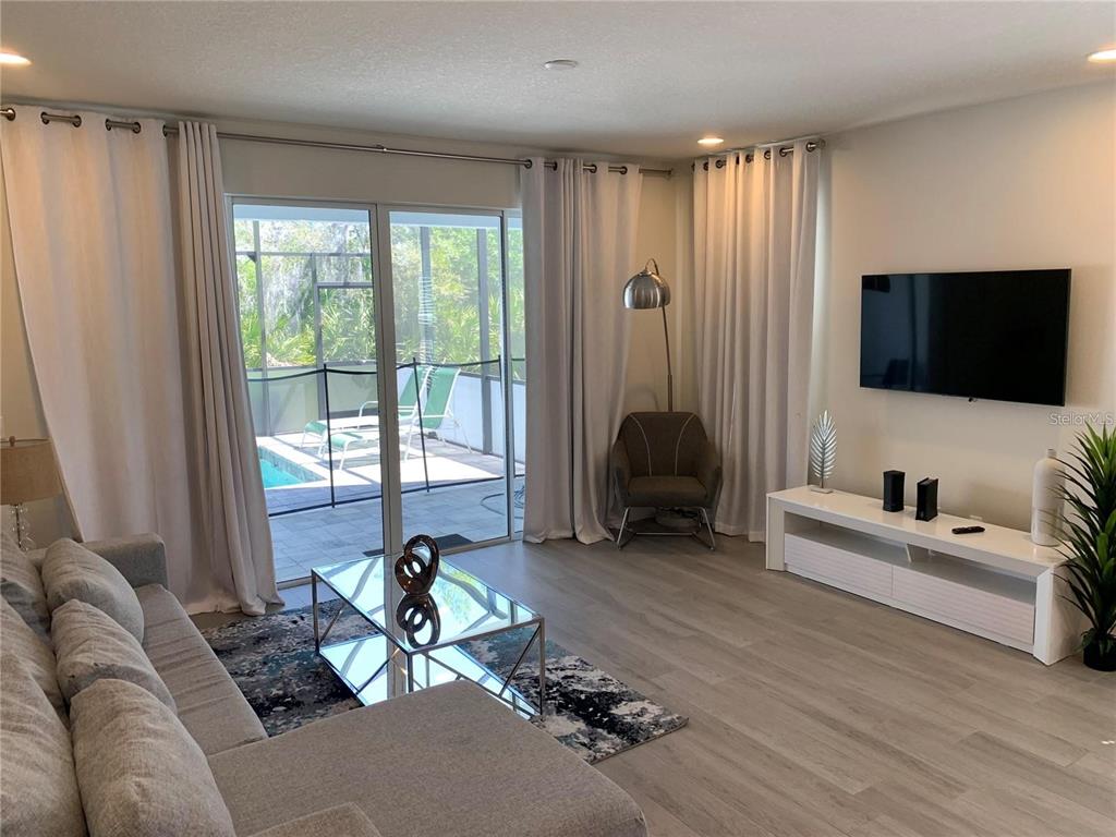 A living room features light wood flooring, a grey sectional, a glass coffee table, and pool views — 17307 HIDDEN FOREST DRIVE, CLERMONT, FL