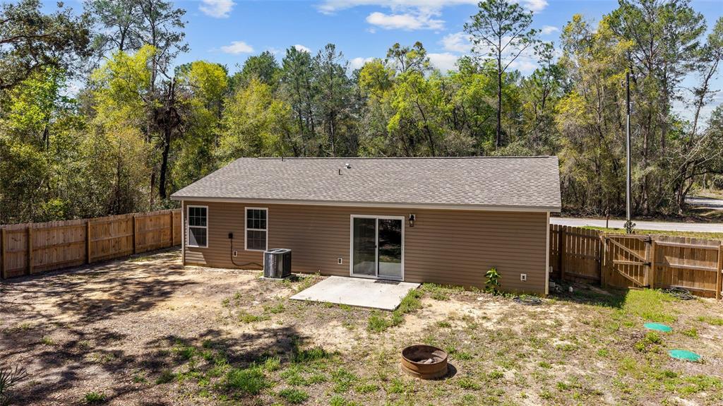 The exterior view shows the back of a tan house with a concrete patio and fence — 23935 NE 118TH AVENUE, FORT MC COY, FL