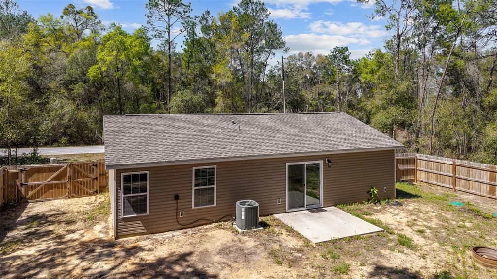 The exterior of a tan house with a concrete patio, sliding glass door, and fenced yard — 23935 NE 118TH AVENUE, FORT MC COY, FL