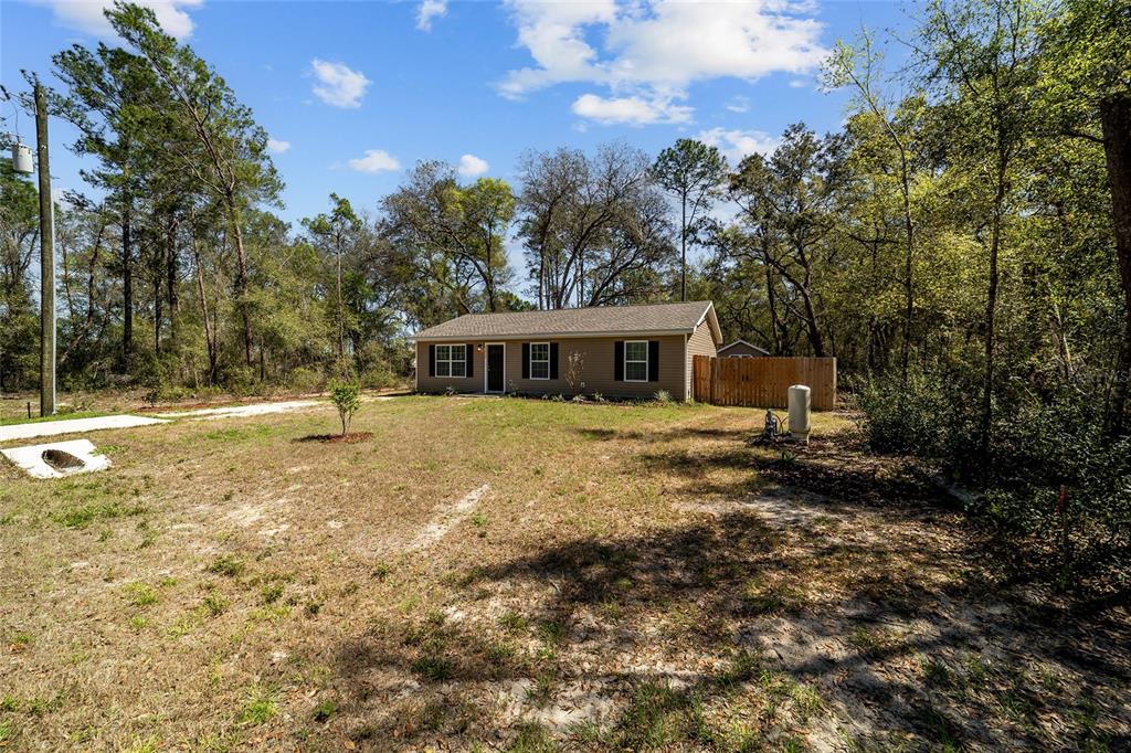 A single-story house with tan siding sits on a large, grassy lot surrounded by trees — 23935 NE 118TH AVENUE, FORT MC COY, FL