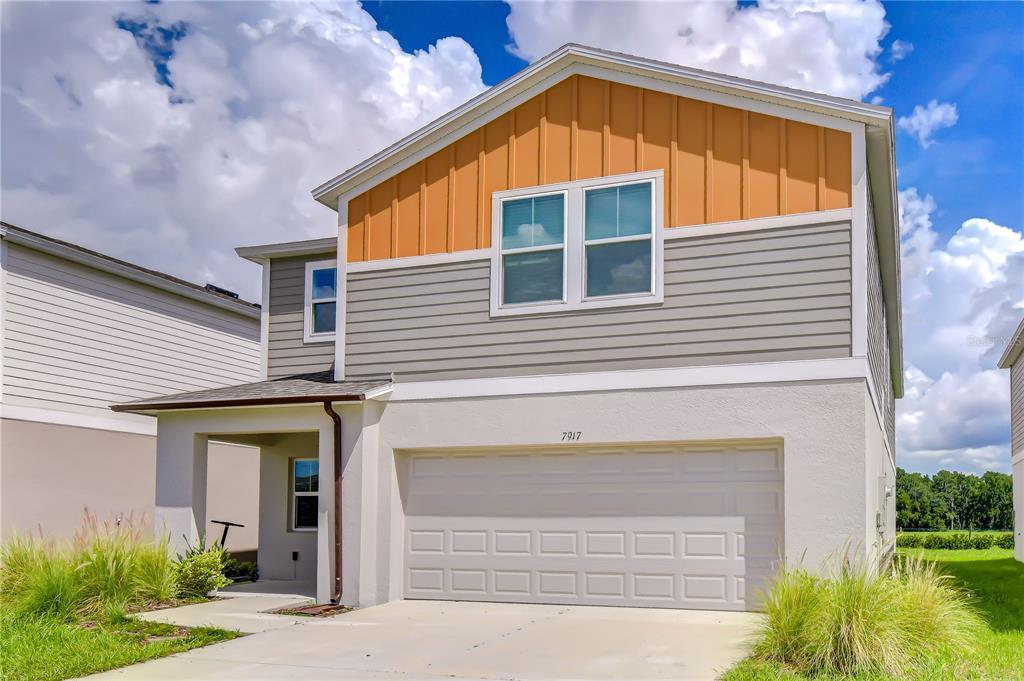 A two-story house features a two-car garage, gray siding, and an orange-paneled gable — 7917 PEACE LILY AVENUE, WESLEY CHAPEL, FL