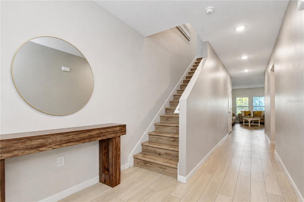 A hallway features light wood-look tile flooring, a wooden console table, and a staircase — 7917 PEACE LILY AVENUE, WESLEY CHAPEL, FL