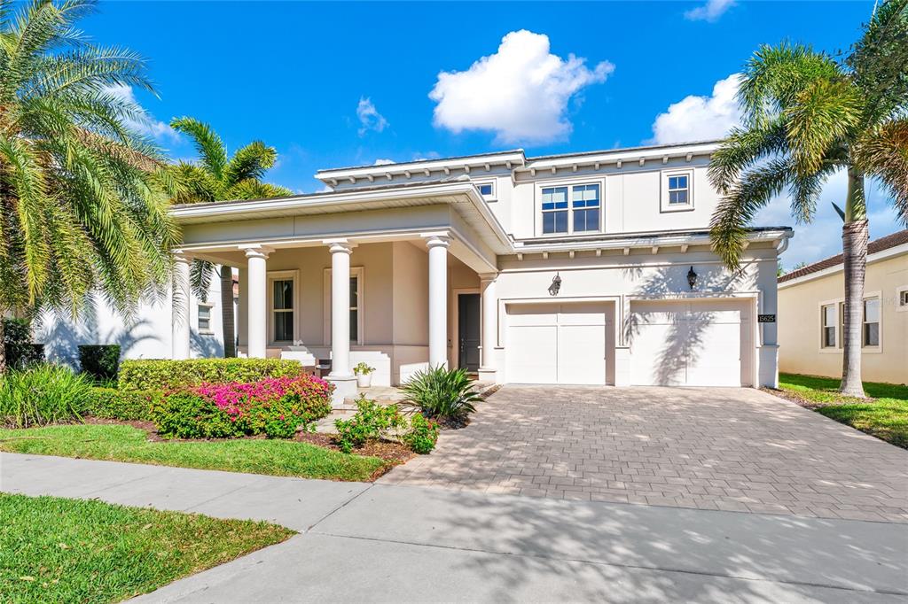 A covered porch features stone pavers, white columns, and wicker chairs beside a potted plant — 15625 SYLVESTER PALM DRIVE, WINTER GARDEN, FL