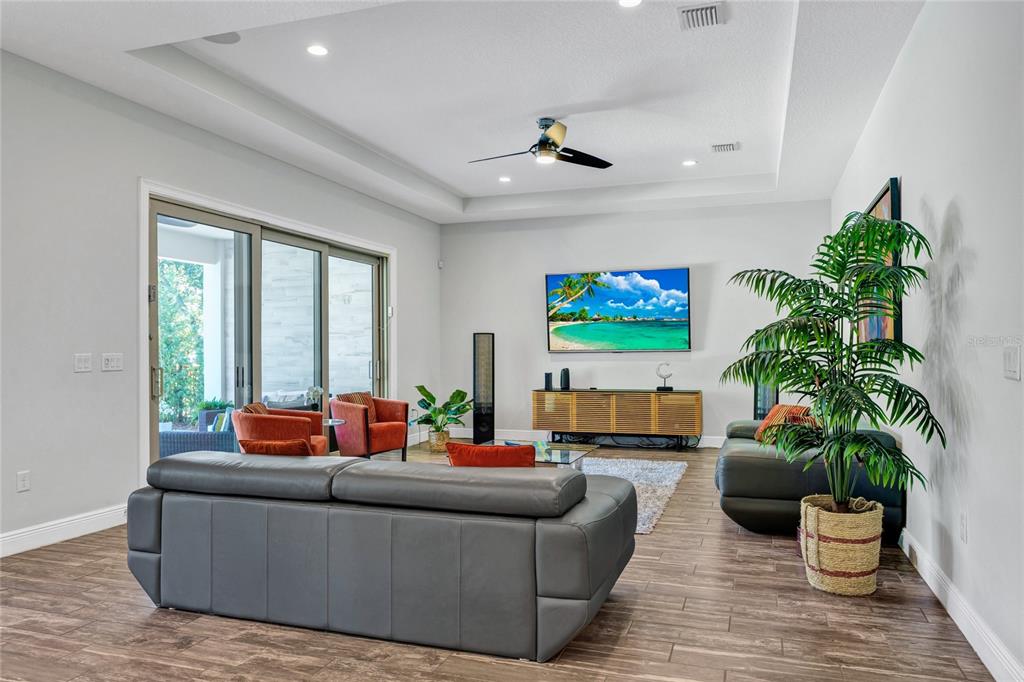 A living room features a gray sectional, orange armchairs, a television, and a sliding glass door — 15625 SYLVESTER PALM DRIVE, WINTER GARDEN, FL