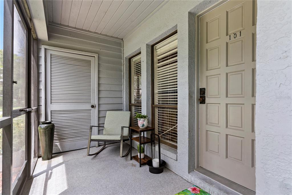 A covered porch features a rocking chair, a small side table, and a front door — 8707 BARDMOOR PLACE UNIT 101, SEMINOLE, FL