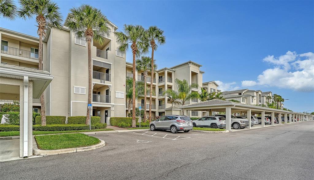 Exterior view of a multi-story apartment building with a covered parking area and palm trees — 1010 TIDEWATER SHORES LOOP UNIT 406, BRADENTON, FL