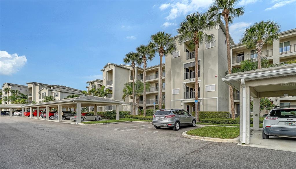 A multi-story apartment building features a parking lot with covered carports and palm trees — 1010 TIDEWATER SHORES LOOP UNIT 406, BRADENTON, FL