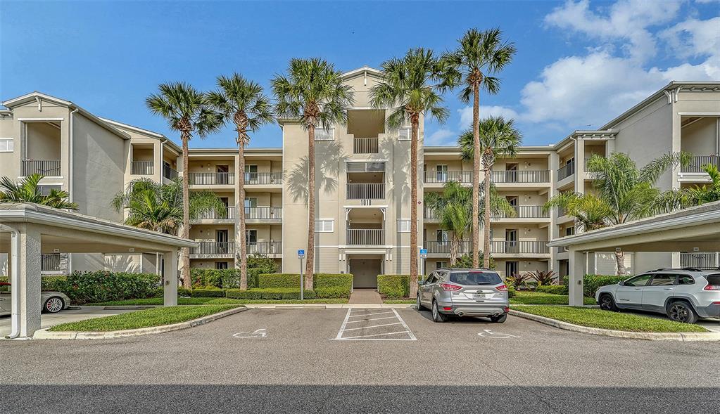 A multi-story apartment building with palm trees, covered parking, and a central entrance — 1010 TIDEWATER SHORES LOOP UNIT 406, BRADENTON, FL