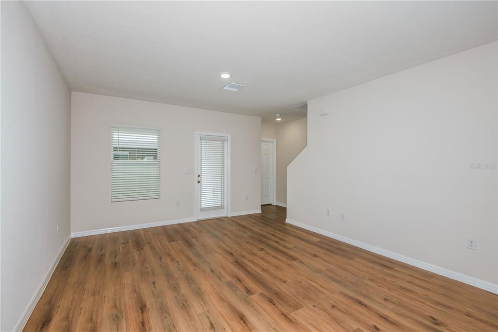 An empty room features light-colored walls, wood-look flooring, a window with blinds, and a glass door — 4255 HILLOCK BOULEVARD, HAINES CITY, FL
