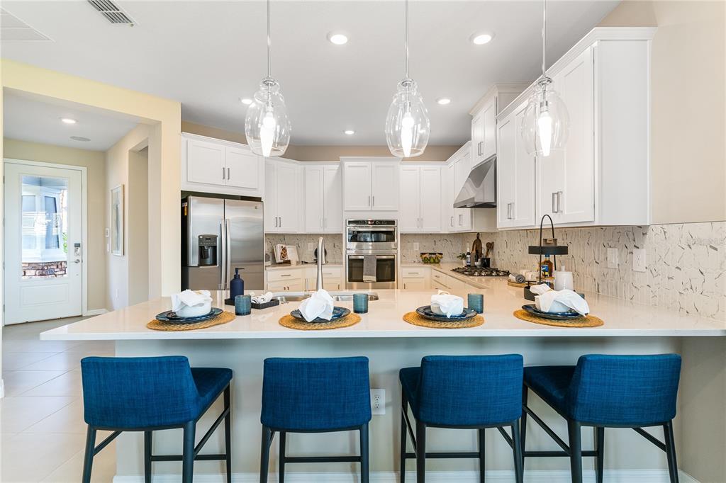 A modern kitchen features white cabinets, stainless steel appliances, a quartz island, and blue stools — 1224 TEAL CREEK DRIVE, ST CLOUD, FL