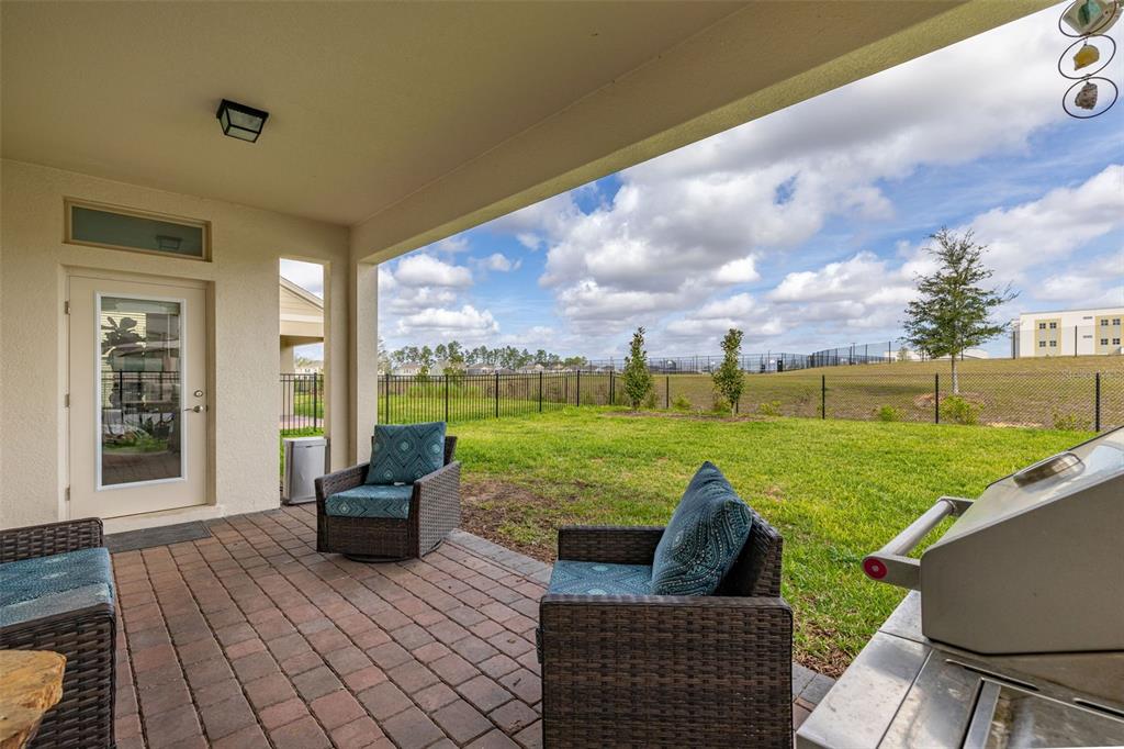 A covered brick patio features outdoor furniture and a grill overlooking a fenced grassy yard — 18339 OLIVER TWIST WAY, WINTER GARDEN, FL