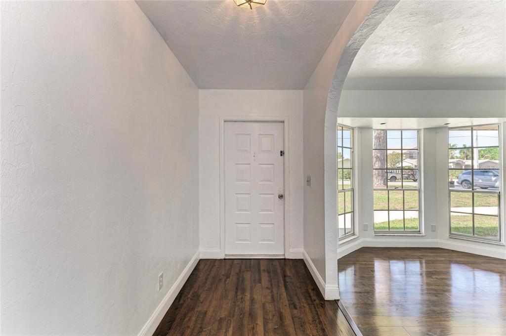 An entryway with white walls and dark wood flooring leads to a white front door — 4404 18TH AVENUE W, BRADENTON, FL