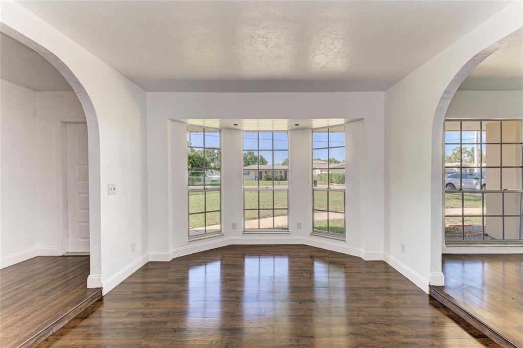 A room with dark wood flooring, white walls, arched doorways, and a large bay window — 4404 18TH AVENUE W, BRADENTON, FL