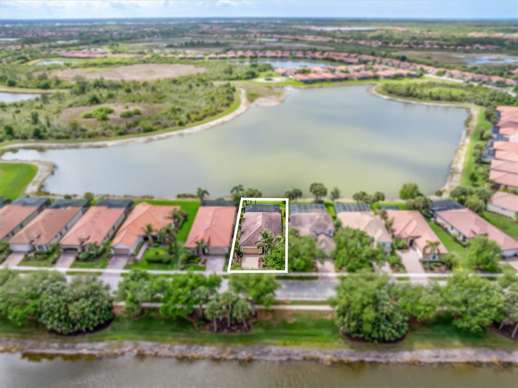 An aerial view shows a single-family home with a screened pool enclosure near a lake — 23126 COPPERLEAF DRIVE, VENICE, FL