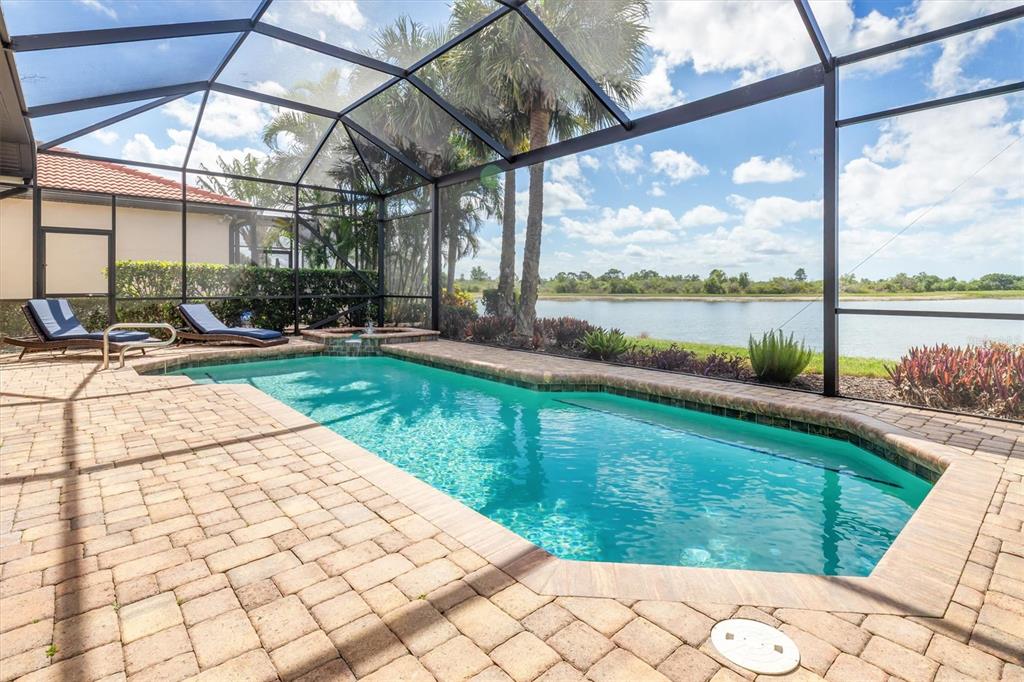 A screened-in swimming pool and spa overlook a lake with palm trees and landscaping — 23126 COPPERLEAF DRIVE, VENICE, FL