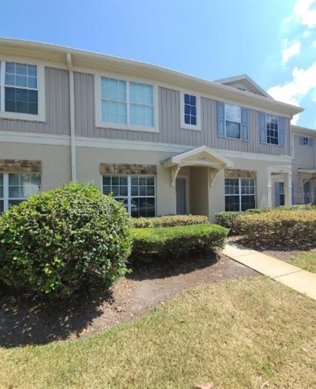 A two-story townhouse exterior features beige stucco, vertical siding, stone accents, and a covered entryway — 15746 STABLE RUN DRIVE, SPRING HILL, FL