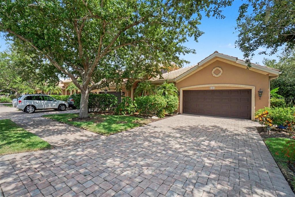 A tan house with a brown garage door and a paved driveway under a large tree — 6103 25TH STREET E, ELLENTON, FL