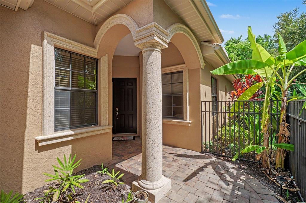 A tan stucco house entrance features a stone column, arched entryway, and a paved walkway — 6103 25TH STREET E, ELLENTON, FL