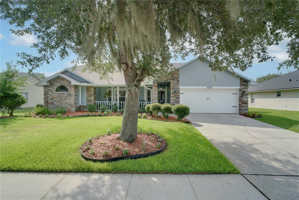 A single-story house with a stone facade, gray siding, a two-car garage, and a large tree — 123 RACHEL LIN LANE, ST CLOUD, FL