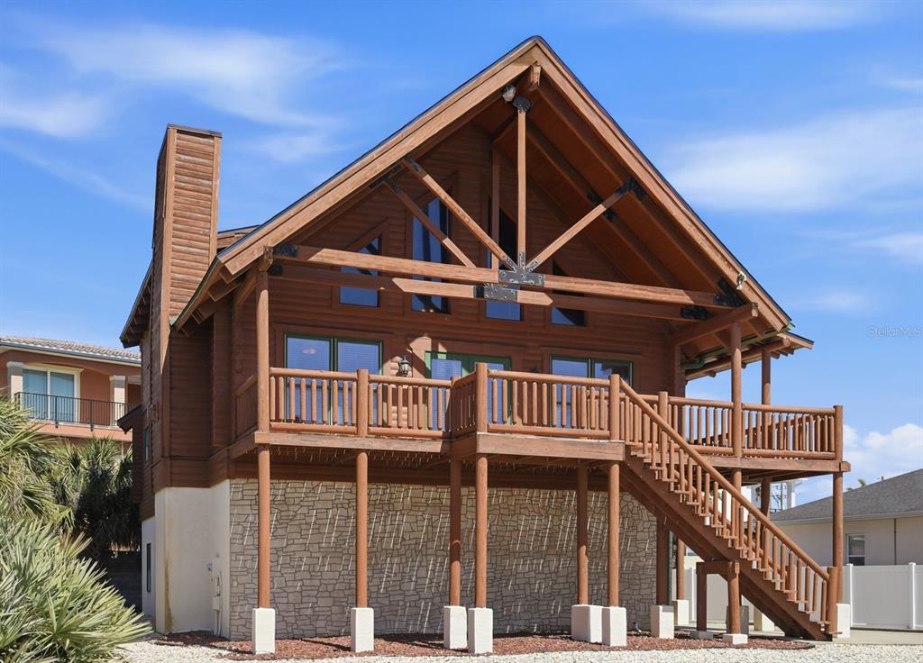 A two-story log cabin home features a large wooden deck and a stone-faced lower level — 109 AVALON DRIVE, ORMOND BEACH, FL