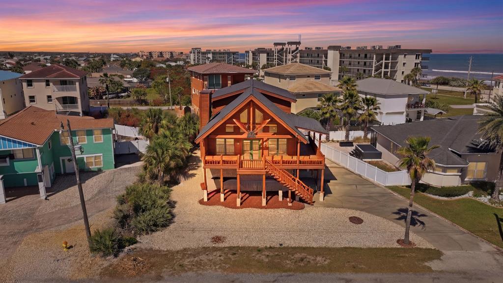 An elevated wooden cabin with a front deck sits between houses near the ocean — 109 AVALON DRIVE, ORMOND BEACH, FL