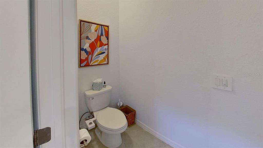 A small bathroom features a white toilet, a wicker wastebasket, and colorful floral wall art — 1505 SADDLEWOOD CIRCLE, PORT CHARLOTTE, FL
