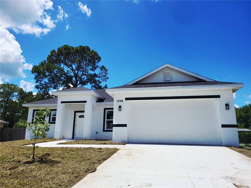 A white single-story house with a two-car garage and a dark roof under a blue sky — 1098 HAMMACHER AVENUE SW, PALM BAY, FL