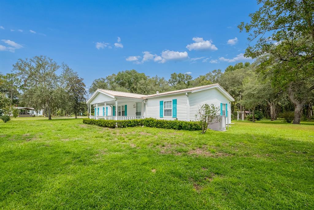 A white single-story manufactured home with blue shutters sits on a large, grassy lot — 17430 NW 80TH COURT, FANNING SPRINGS, FL