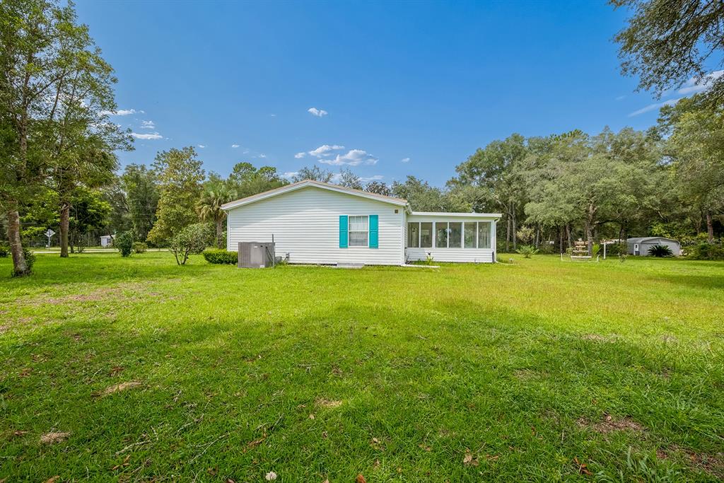 A white single-story house with a sunroom sits on a large, grassy lot with trees — 17430 NW 80TH COURT, FANNING SPRINGS, FL