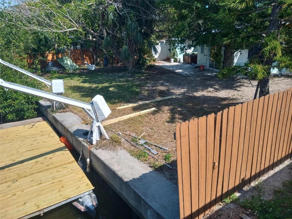 A backyard features a wooden dock with a boat lift, a concrete seawall, and fencing — 6631 ROSATI LANE S, ST PETERSBURG, FL