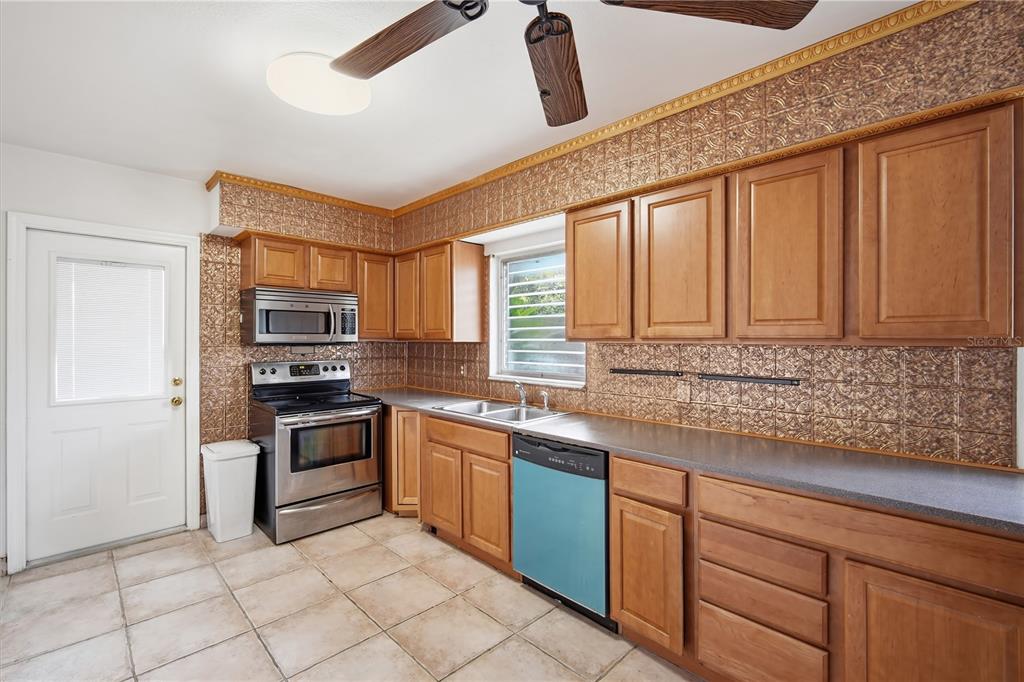 A kitchen features wood cabinets, stainless steel appliances, a blue dishwasher, and copper-colored backsplash tiles — 3106 W BRADDOCK STREET, TAMPA, FL
