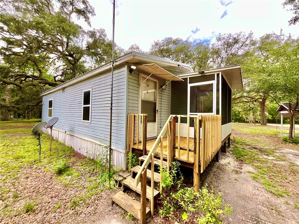 An exterior view of a light blue mobile home with a wooden deck and screened porch — 107 CRYSTAL LAKE DRIVE, MELROSE, FL