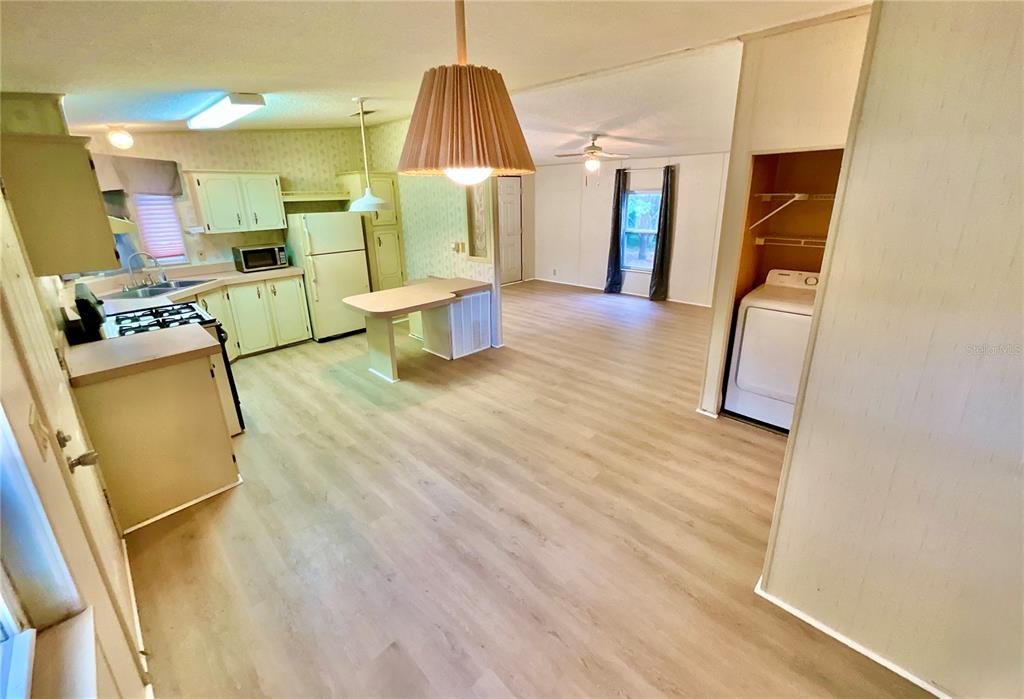 A kitchen with light wood-look flooring opens into a living area with a laundry closet — 107 CRYSTAL LAKE DRIVE, MELROSE, FL