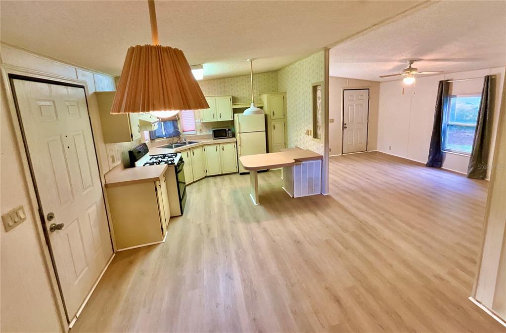 An open-concept kitchen with light wood-look flooring flows into an adjacent living area — 107 CRYSTAL LAKE DRIVE, MELROSE, FL
